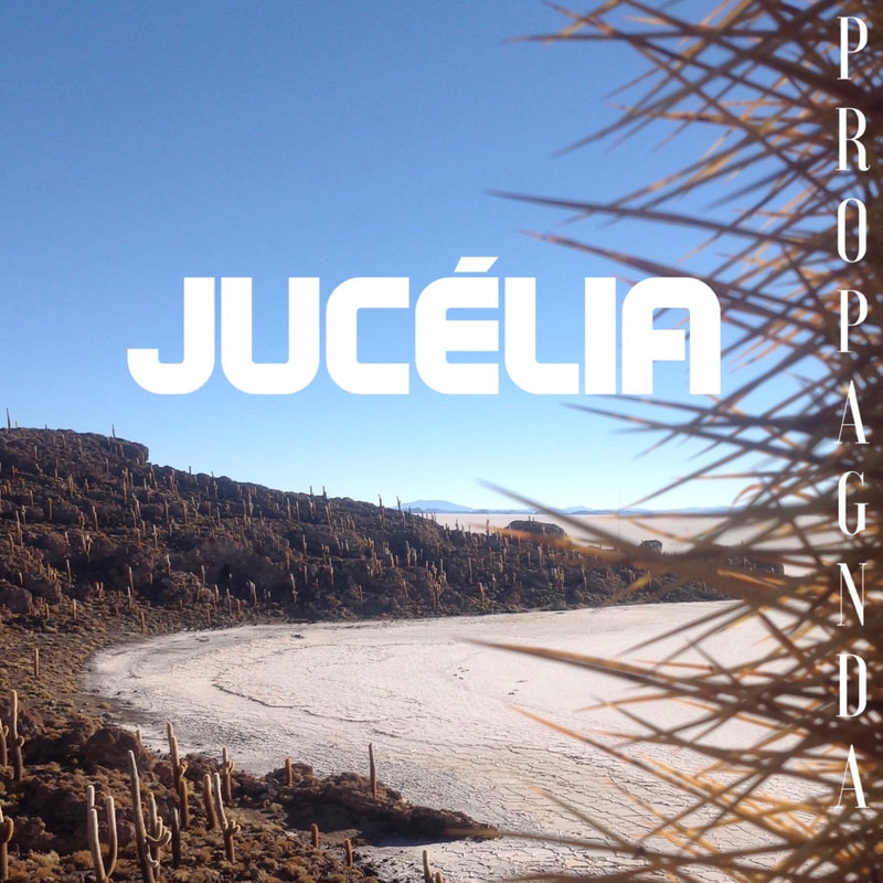 The cover art for the song Jucelia by PROPAGNDA features the name Jucelia centered in bold, solid white on an unblemished blue sky, hovering over a desert landscape oasis riddled with cacti. There is an especially prominent cactus bordering the right side of the photograph with sinister-looking spines and a subtle 